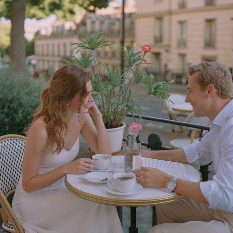 Elise en Thomas lachen samen aan een tafeltje op een zonnig caféterras