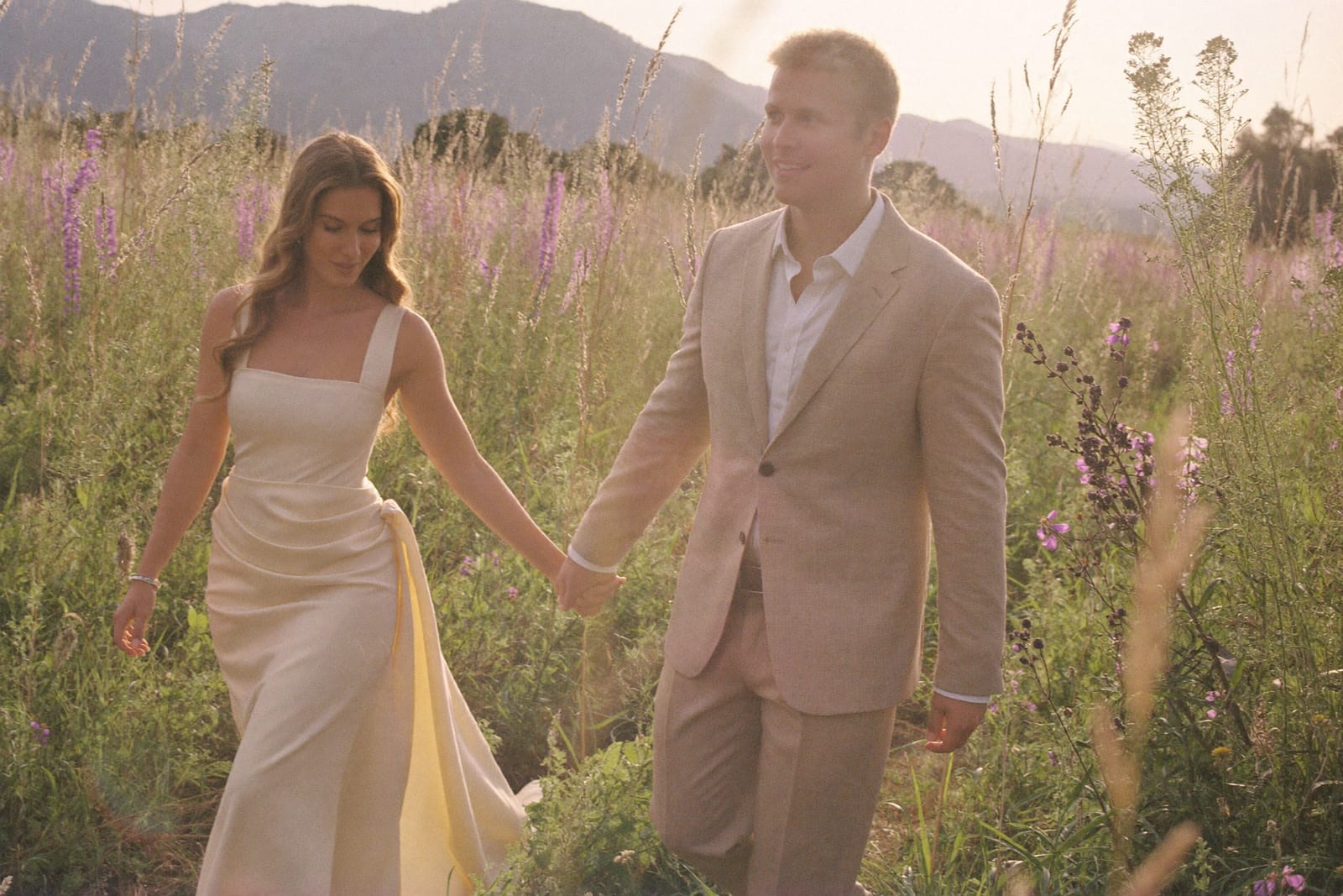 Verlovingsshoot: Elise en Thomas wandelen hand in hand door een bloemenveld bij zonsondergang